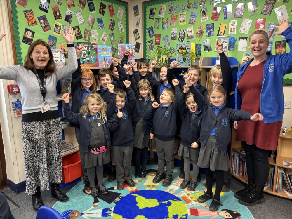 The Headteacher stands with pupils in the school library - all with a big thumbs up